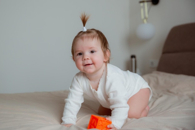 The baby girl is sitting at home on the bed in the bedroom playing with cubes