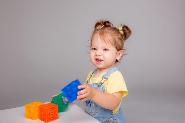 baby girl is sitting on a white background and playing with colorful cubes. kid's play toy cube