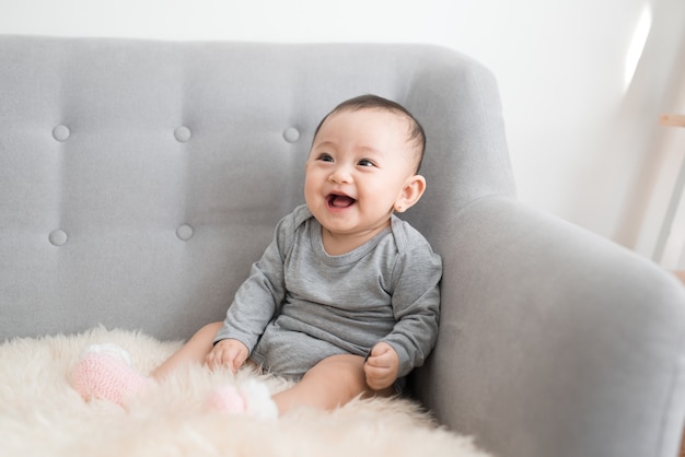 Baby girl is smiling and sitting on sofa in jumpsuit