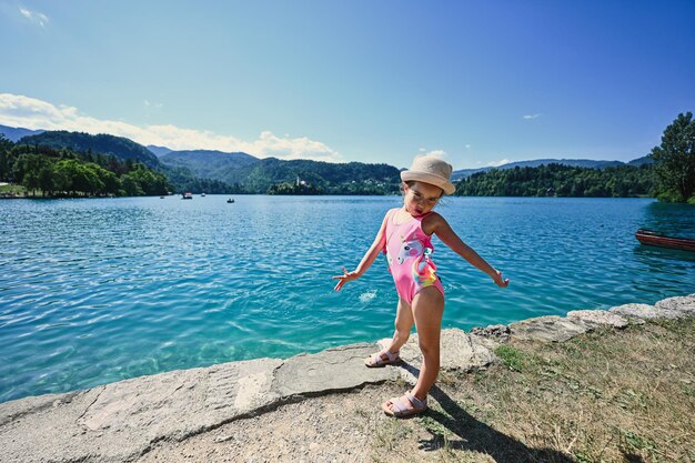 Baby girl is swimsuit and hat posed in pier of view beautiful Bled Lake Slovenia