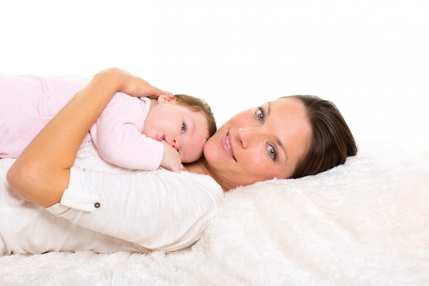 Baby girl and mother lying happy together on white fur