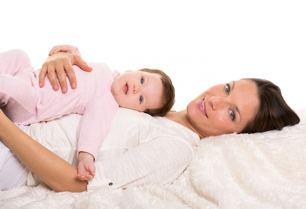 Baby girl and mother lying happy together on white fur