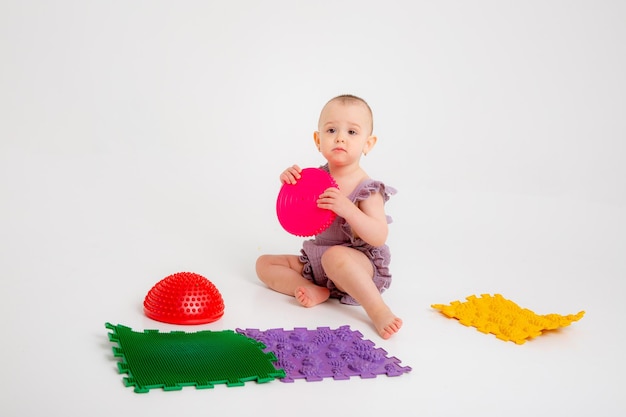 Baby girl on orthopedic massage mat on white background Massage of children's legs