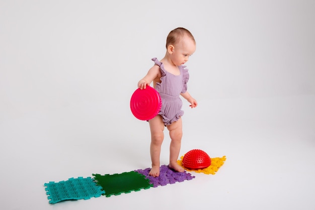 Baby girl on orthopedic massage mat on white background Massage of children's legs