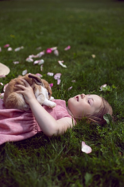 Baby girl in a pink dress plays with a rabbit in a green meadow in summer Funny friendship between a child and an animal during Easter