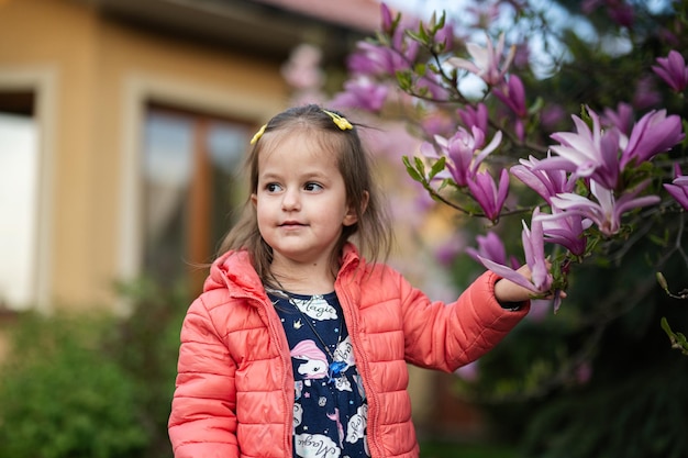 Baby girl in pink jacket enjoying nice spring day near magnolia blooming tree Springtime activities