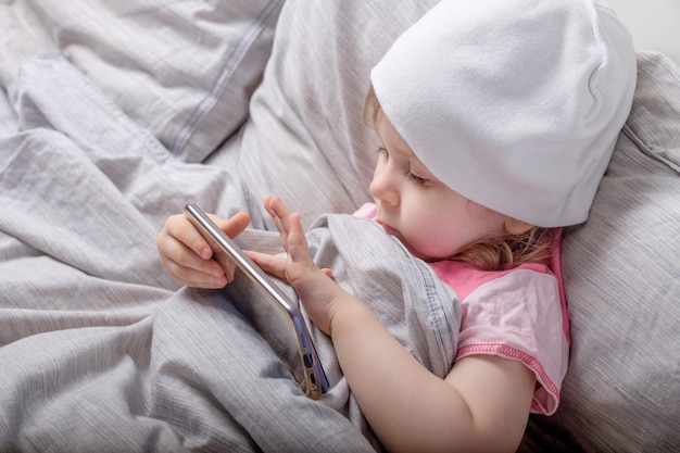 Baby girl playing with smartphone on the bed