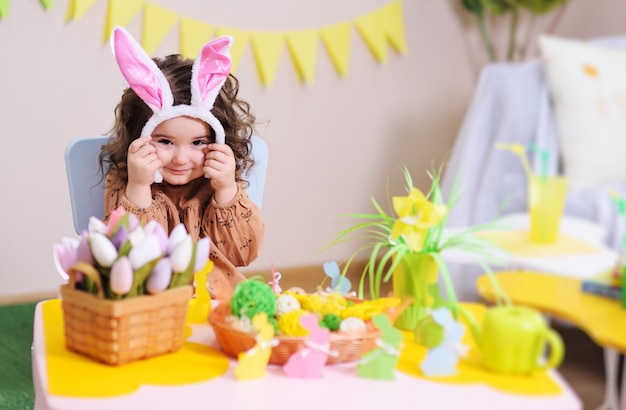 Baby girl in rabbit ears sitting at table on surface of Easter decor