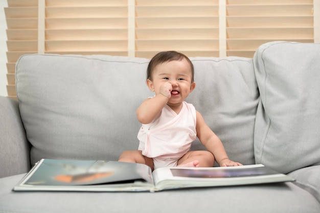 Baby girl reading a book sitting on sofa at home