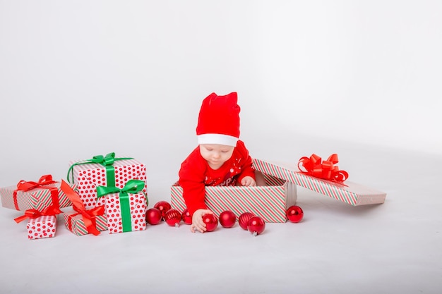 A baby girl in a Santa costume with gifts on a white background Santa Claus Helper