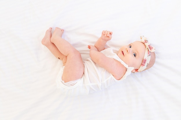 Baby girl smiling lying on a white cotton bed at home on her back