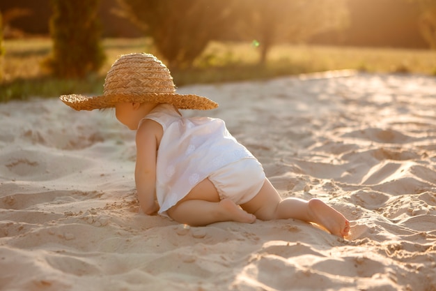 baby girl in white clothes playing on a sandy beach in summer