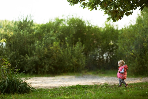 Baby girl with blond hair wearing pink waistcoat walking in green park exploring the big and interesting world