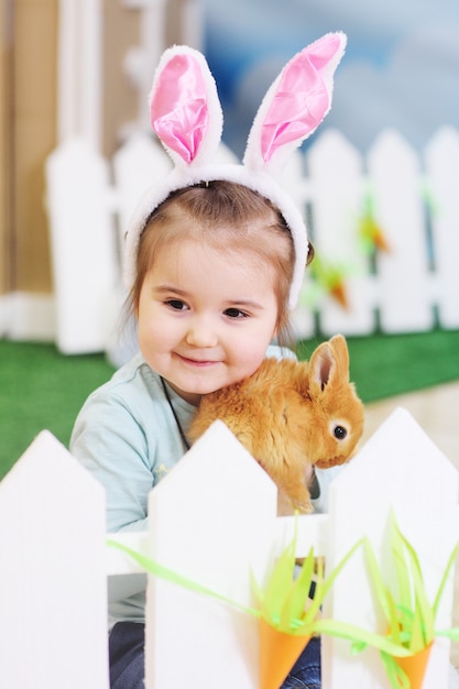 Baby girl with Bunny ears holding a small red fluffy rabbit. Easter concept