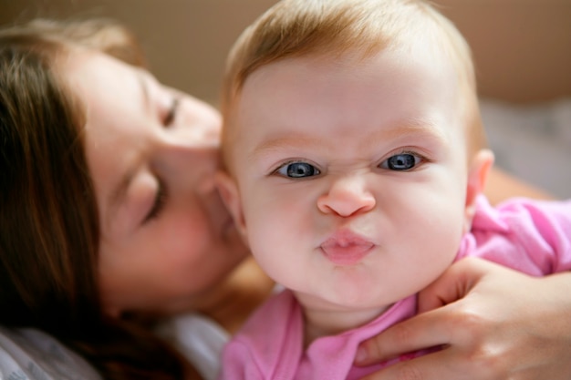 baby girl with funny expression in her face kissed by her big sister