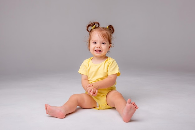 Baby girl with yellow bodysuit sitting on a white background