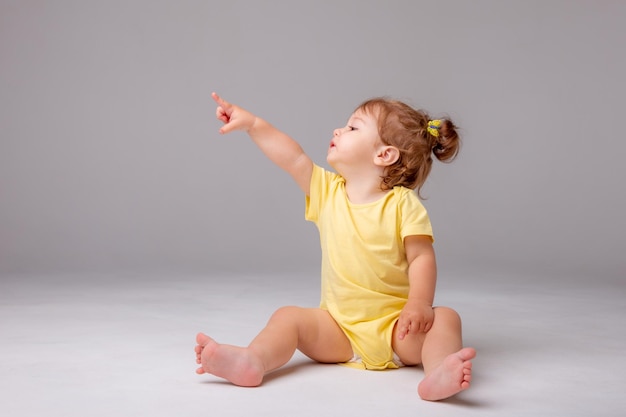 Baby girl with yellow bodysuit sitting on a white background