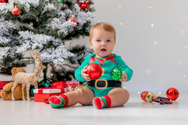 Baby in green bodysuit holds colorful Christmas balls in his hands. kid in a Christmas gnome costume. winter New Year's concept. holiday goods. space for text. High quality photo