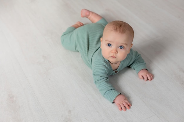 baby in a green cotton jumpsuit learns to crawl on the floor child development place for text