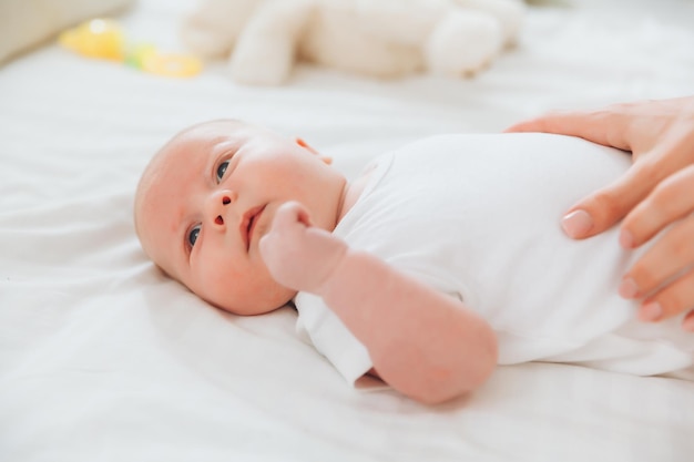 The baby is lying on the bed for 2 months the mother's hand on the baby's stomach newborn baby