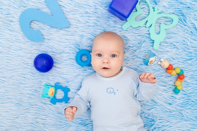 The baby is lying on a blue Mat at home among the toys, the concept of development and games