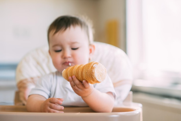 The baby in the kitchen greedily eats delicious creamy tubes filled with vanilla cream