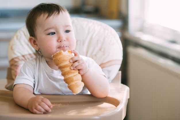 The baby in the kitchen greedily eats delicious creamy tubes filled with vanilla cream