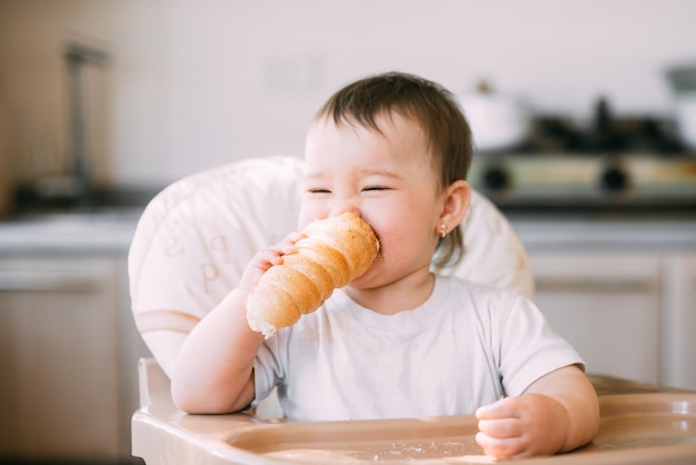 The baby in the kitchen greedily eats delicious creamy tubes filled with vanilla cream