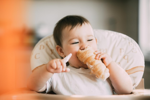 The baby in the kitchen greedily eats delicious creamy tubes filled with vanilla cream