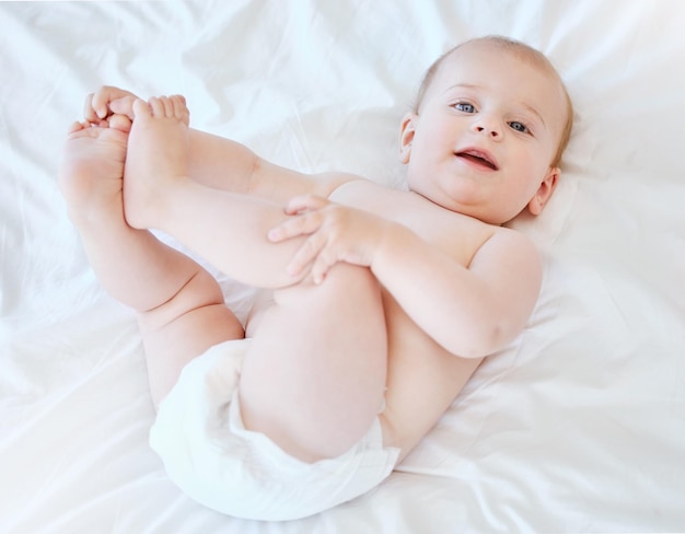 Baby legs and portrait on bed for development relax and game or learning in home Child wake up and smile in nursery for motor skills and face in morning for play wellness and healthy for growth