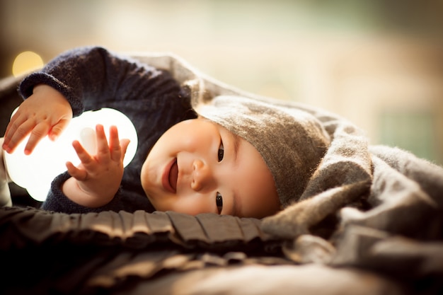 A baby lying on a grey cushion is enjoying sitting the doll and smiling brightly.