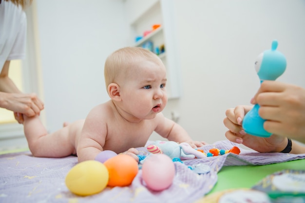 A baby lying on his stomach gets a massage in a massage room his mother distracts him with a toy