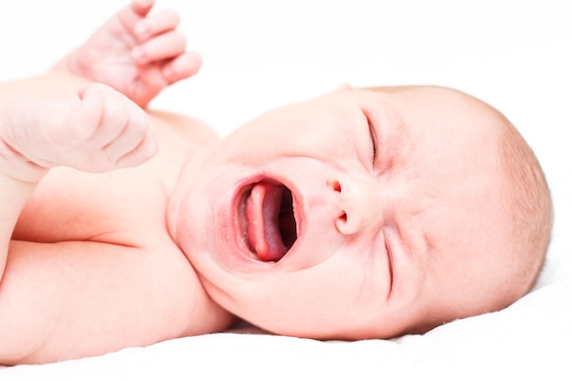 The baby naked lies on her back on a white sheet and shows emotions Selective focus on the baby39s head The child looks directly at the camera Closeup