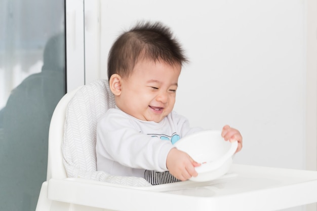 Baby playing plastic bowl while waiting for breakfast