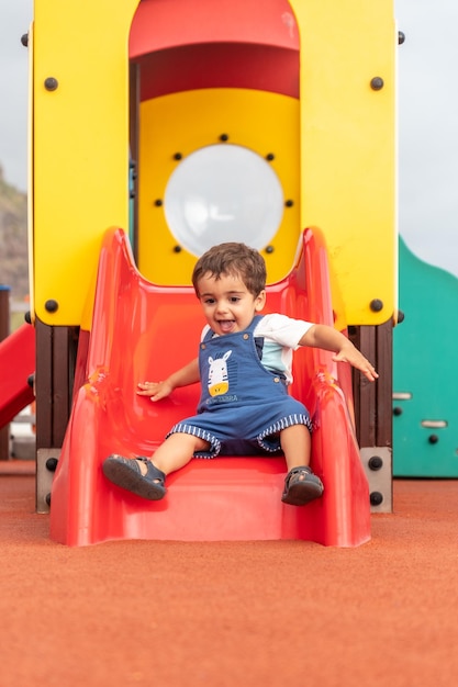 Baby playing in a playground having fun in summer adapted park going down a small squeaker