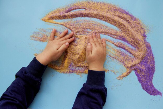 Baby plays with colorful sand Child fine motor skills development Creative kids occupation View from above