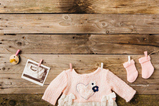 Baby's dress; socks; pacifier and sonography picture hanging on clothesline with clothespins against wooden wall