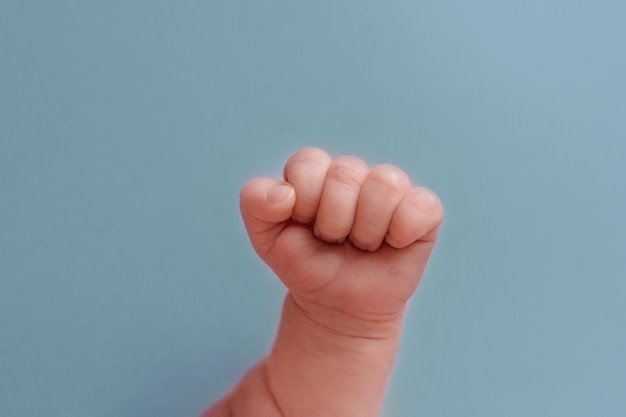 A baby's fist is held up against a blue background.