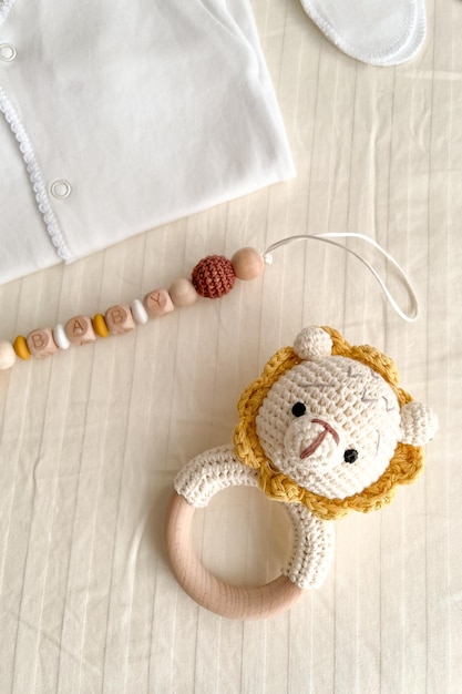 A baby's white suit a hat for a newborn scratches socks a rattle with a lion and a chain of wooden beads for teeth are lying on the bed vertical photo