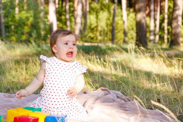 the baby screams very loudly with her mouth wide open in the park on a summer day