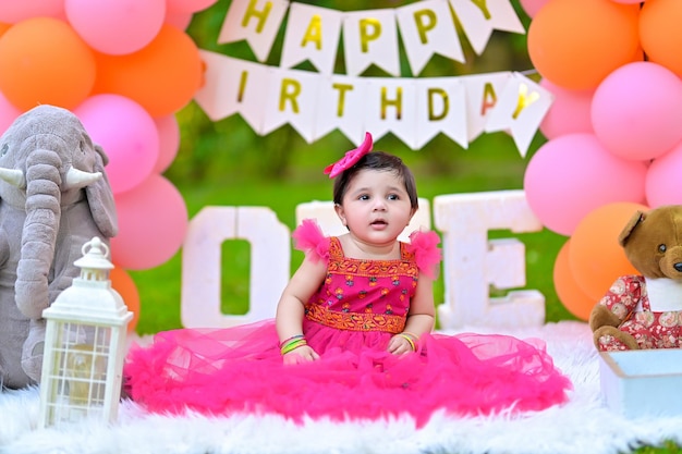 a baby sits in a bed with balloons and a banner that says happy birthday