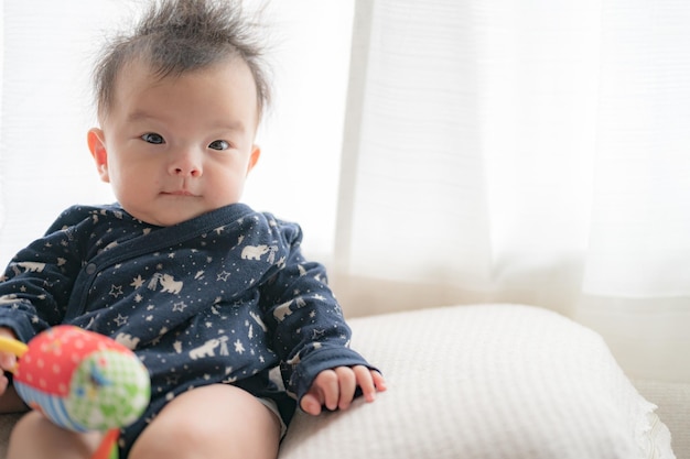 A baby sits on a couch with a toy in his hand.