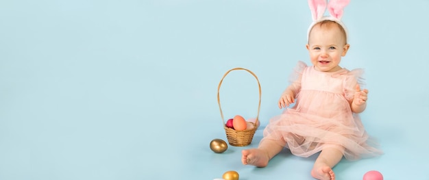 A baby sits in front of a blue background with easter eggs.