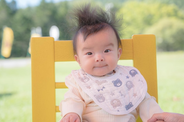 A baby sits on a yellow chair with a white bib that says'baby'on it