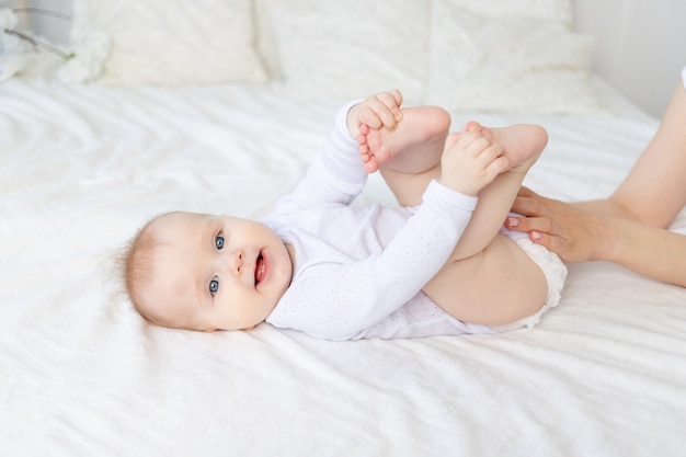 A baby six months old with his mother's hands on a white cotton bed at home smiling or laughing