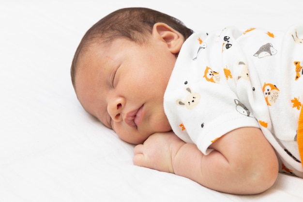 Baby sleeping in bed with his arms under his head.