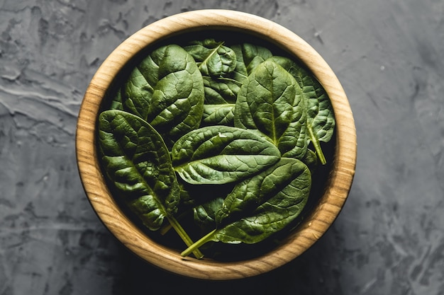 Baby spinach leaves in bowl on grey concrete background, top view, copy space. Clean eating, detox, diet food ingredient