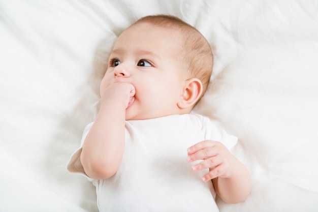 The baby teething Close up portrait of little baby girl in white lying on a white bed