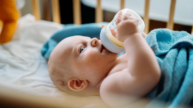 Baby toddler laying on the blue blanket drinks milk from bottle Cover photo