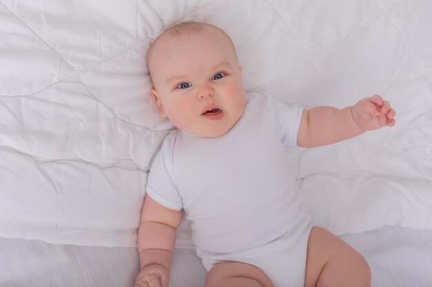 baby in a white bodysuit is lying on his back in a white bed kid plays with his toes